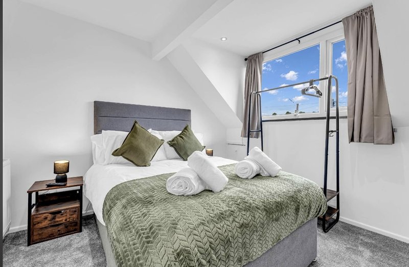 Bright bedroom with double bed, green bedding, olive cushions, wooden nightstand, and skylight window