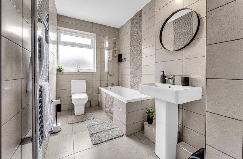 Modern bathroom with white pedestal sink, bathtub, toilet, heated towel rail and round mirror