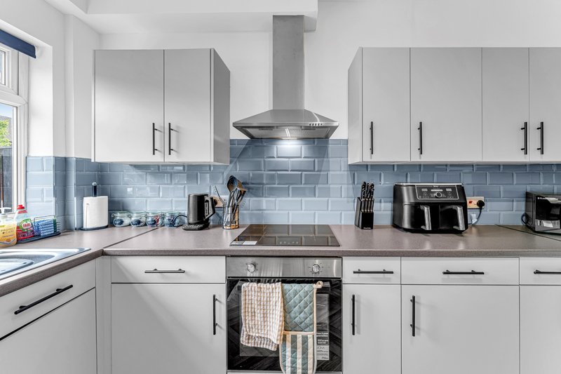 Modern kitchen with white cabinetry, blue subway tile backsplash, stainless steel range hood and appliances