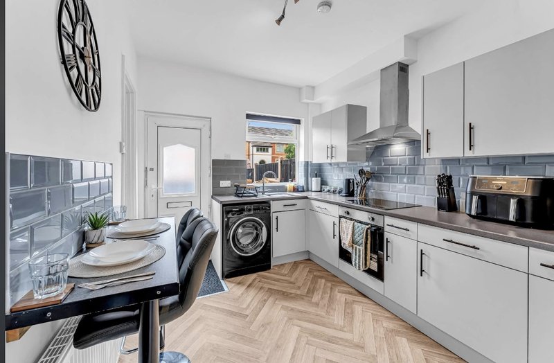 Modern kitchen with white cabinets, blue tile backsplash, dining table and herringbone wood flooring