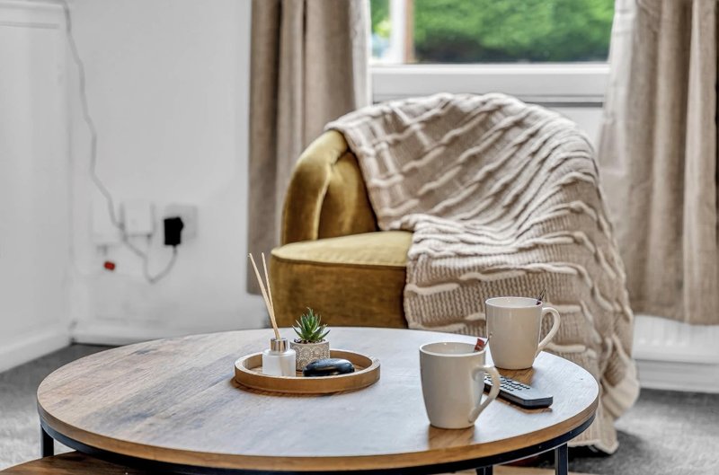 Modern living room with round marble table, two mugs, armchair with throw blanket and green garden view