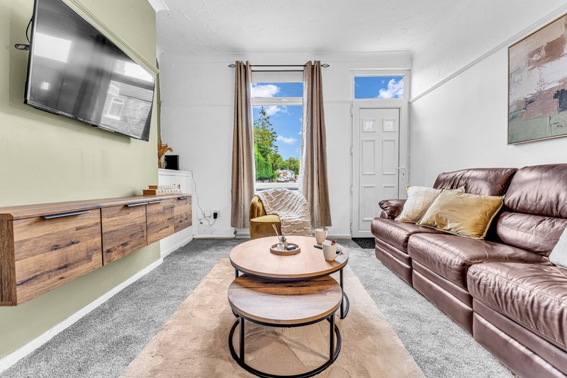 Bright living room with leather sofa, wooden TV unit, nesting tables and garden view through patio doors