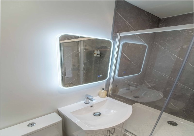 Modern bathroom with illuminated mirror, white sink, and glass shower enclosure