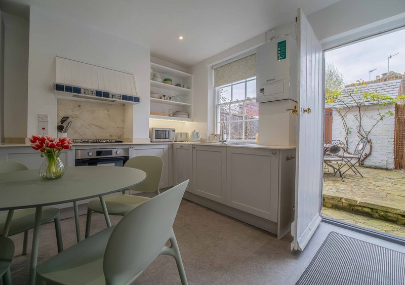 Modern kitchen-diner with sage cabinetry, round table, chairs and garden view through patio doors