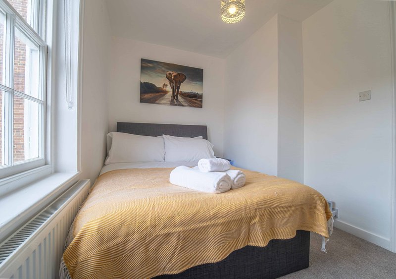 Bright bedroom with double bed, golden throw, white towels and landscape artwork