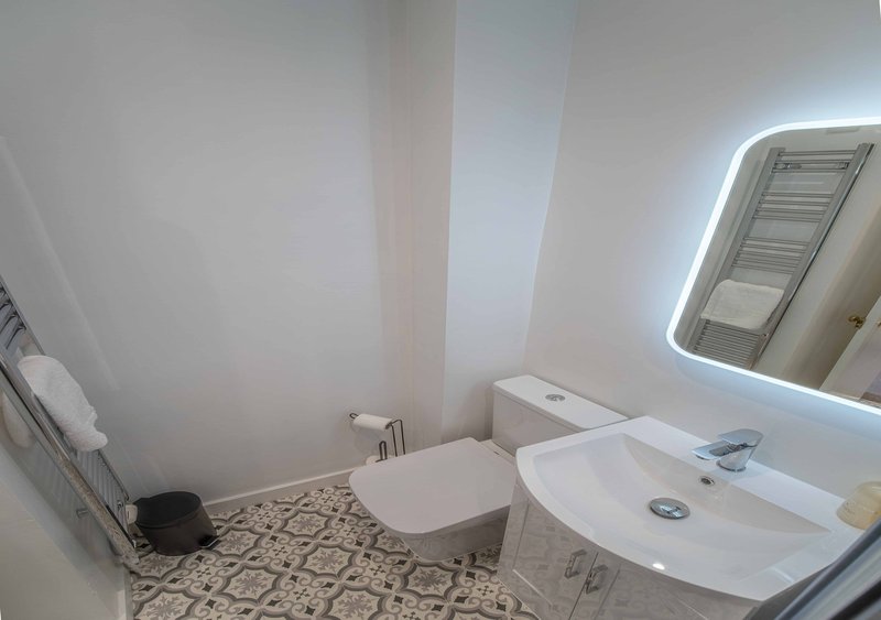 Modern bathroom with white vanity, illuminated mirror, toilet and patterned floor tiles