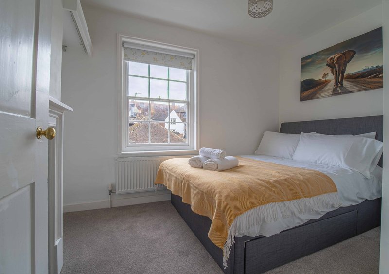 Bright bedroom with double bed, yellow throw, white pillows, window and framed wall art