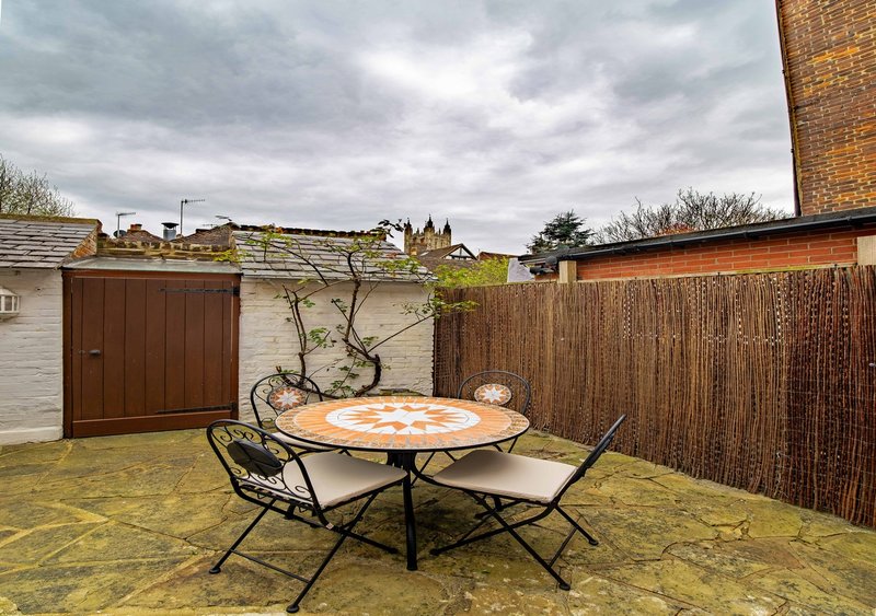 Paved garden with round patio table, chairs, fencing, shed and neighbouring properties visible