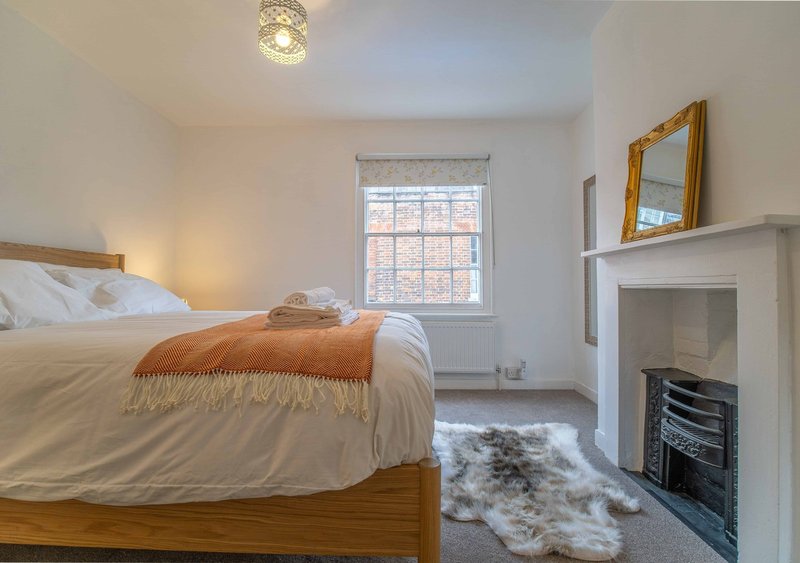Bedroom with wooden bed, white bedding, orange throw, fireplace and gold-framed mirror