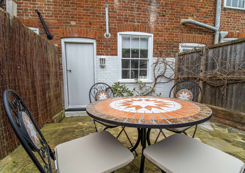 Brick courtyard with round patterned table, chairs, white door and wooden fence