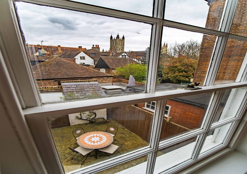 Window view of residential rooftops, garden with round table, and distant church spire
