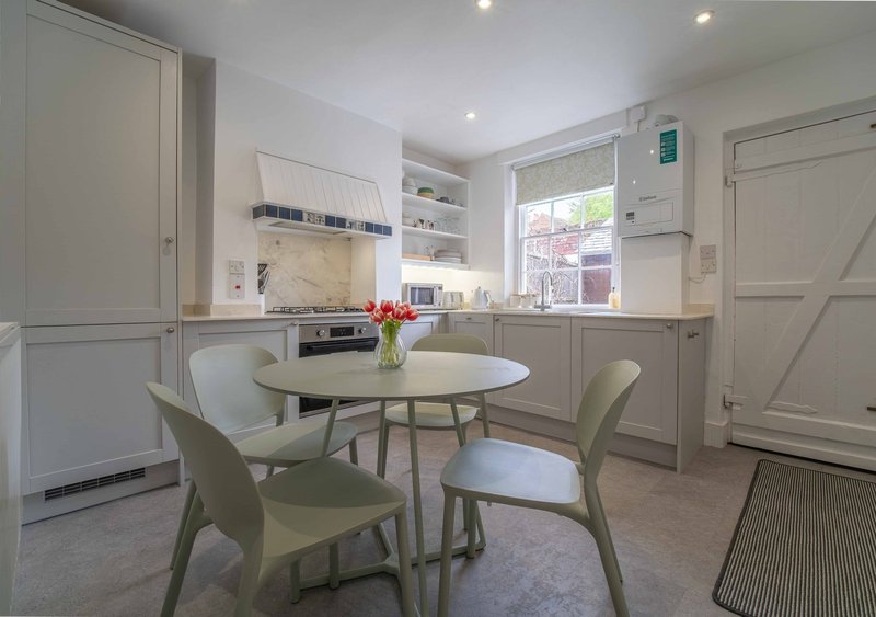 Modern kitchen-diner with white cabinetry, round dining table, green chairs and flowers