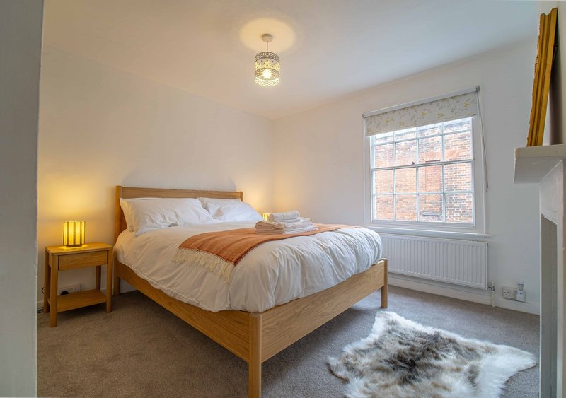 Bright bedroom with wooden bed, white bedding, wooden nightstand, and window with natural light