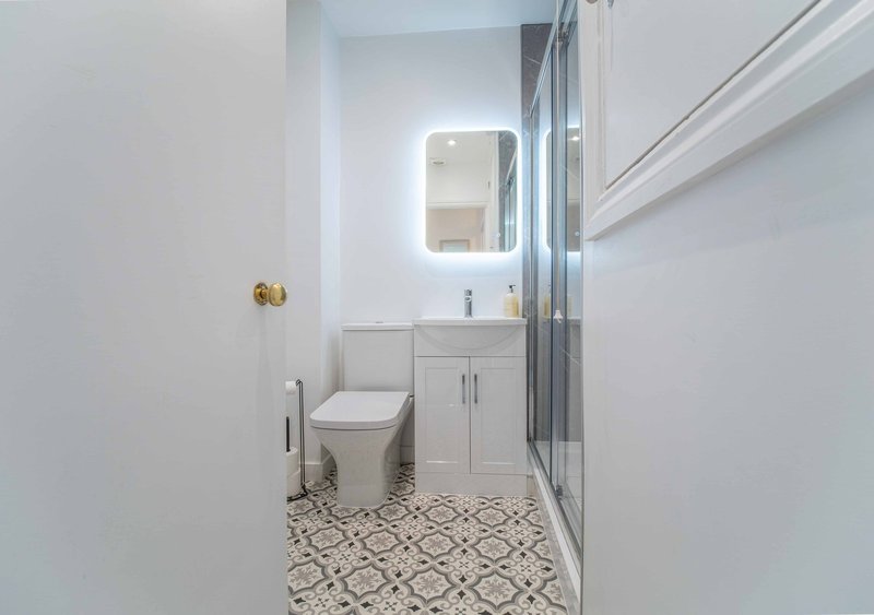 Modern bathroom with white vanity, illuminated mirror, toilet, and patterned floor tile