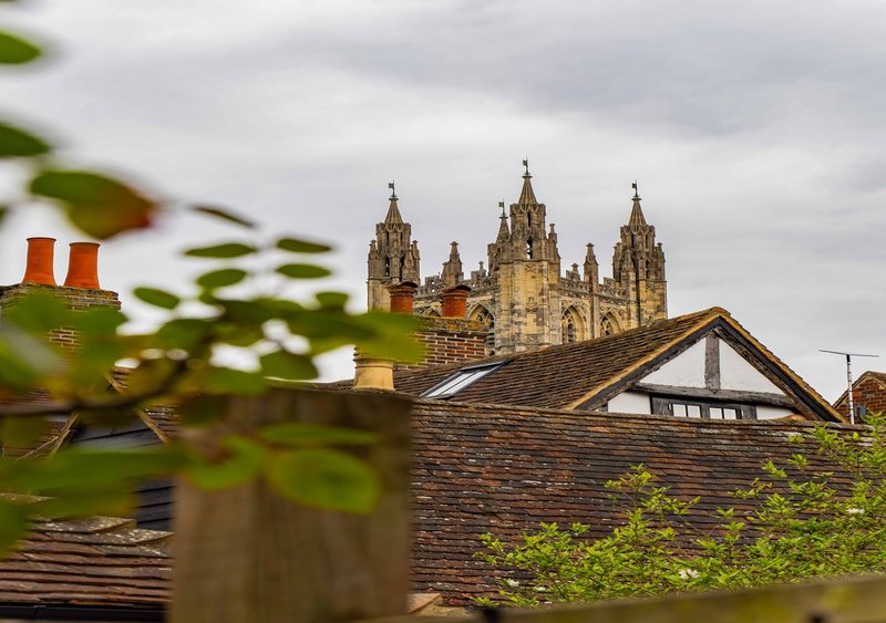 Gothic stone cathedral with multiple spires visible beyond residential roofline and garden foliage