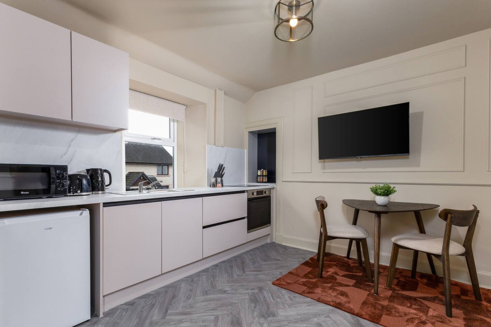 Modern open-plan kitchen and dining area with white cabinetry, dining table, and wall-mounted TV