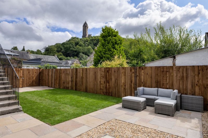 Garden with lawn, wooden fence, patio seating and historic tower visible in background