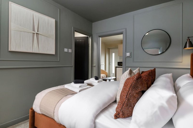 Modern bedroom with twin beds, grey walls, round mirror and contemporary artwork