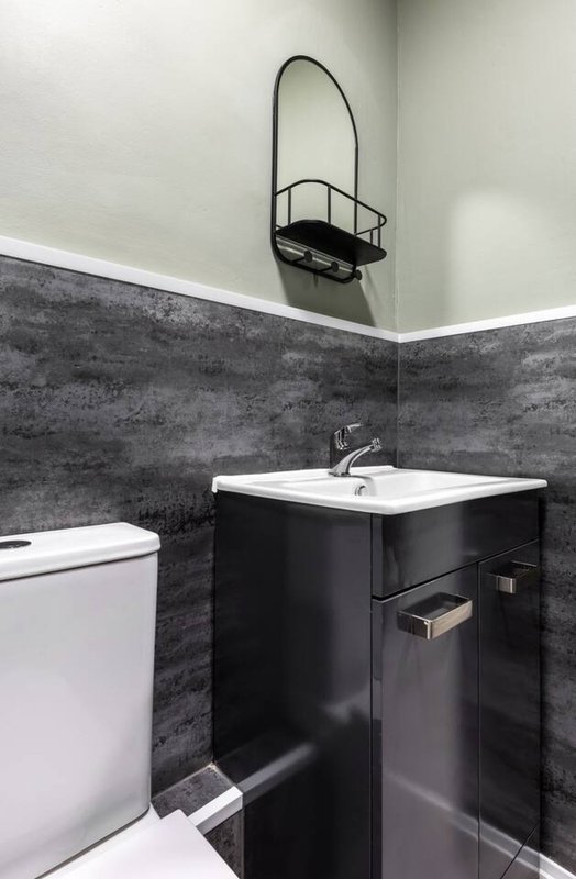 Modern bathroom with black vanity sink, white toilet, dark tile walls and arched mirror