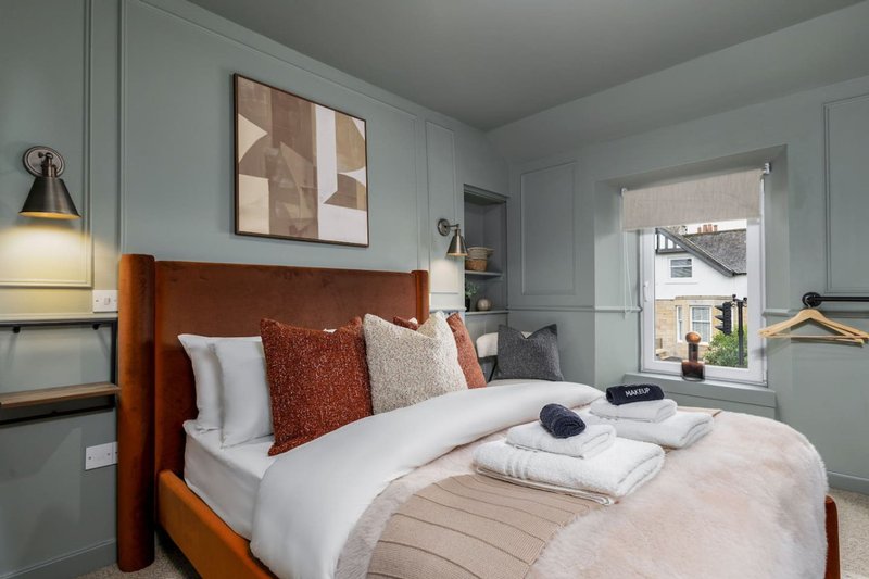 Modern bedroom with orange upholstered bed, white bedding, decorative pillows and folded towels