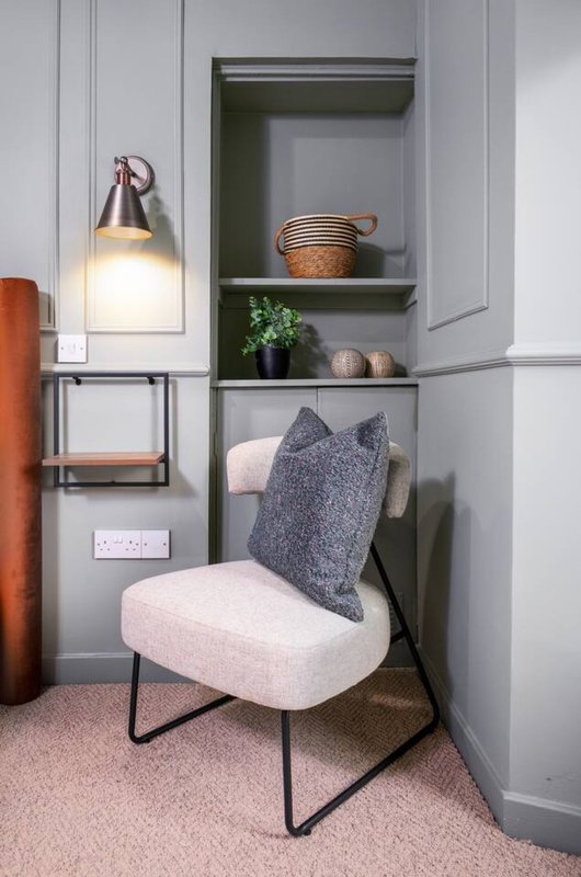 Modern bedroom nook with cream chair, built-in shelving, pendant lamp, and decorative cushion