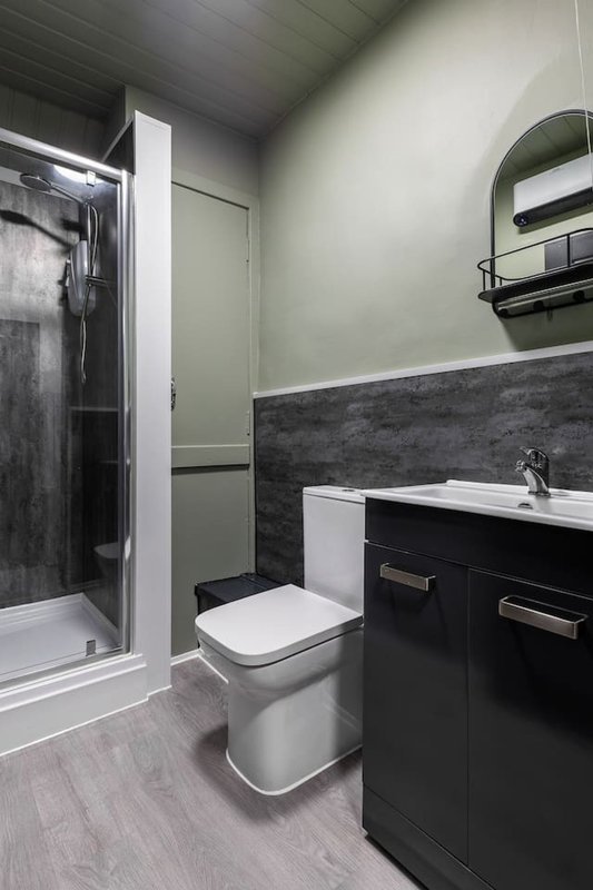 Modern bathroom with shower enclosure, toilet, dark vanity unit and round mirror