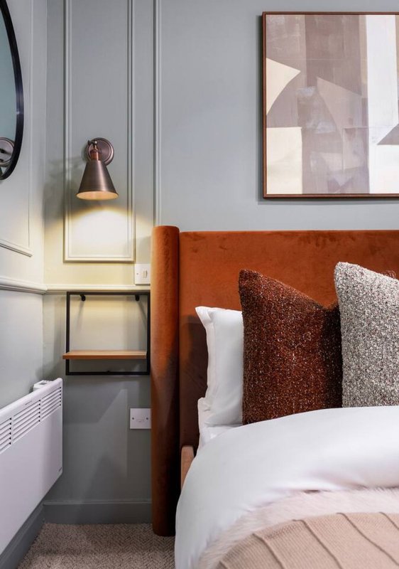 Modern bedroom with orange headboard, white bedding, brown cushions, pendant lamp and framed artwork