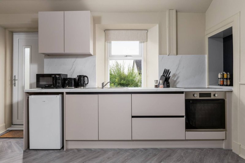 Modern kitchen with pale grey cabinetry, marble backsplash, built-in oven and window view