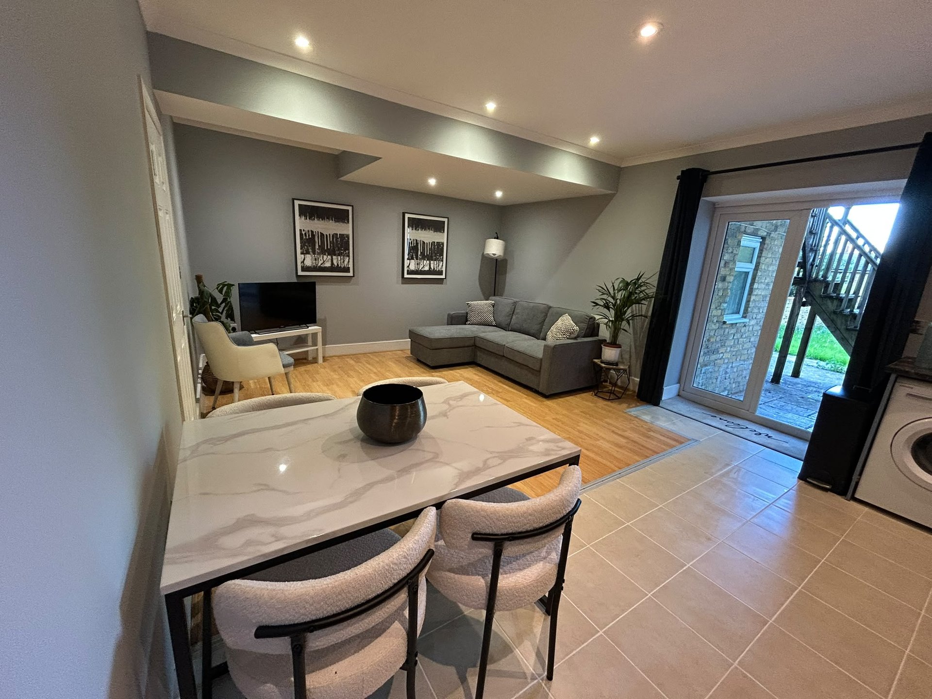 Open-plan living area with dining table, sofa, TV, wooden flooring and modern lighting