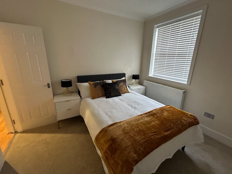 Modern bedroom with double bed, brown throw, cushions, bedside tables and window blinds