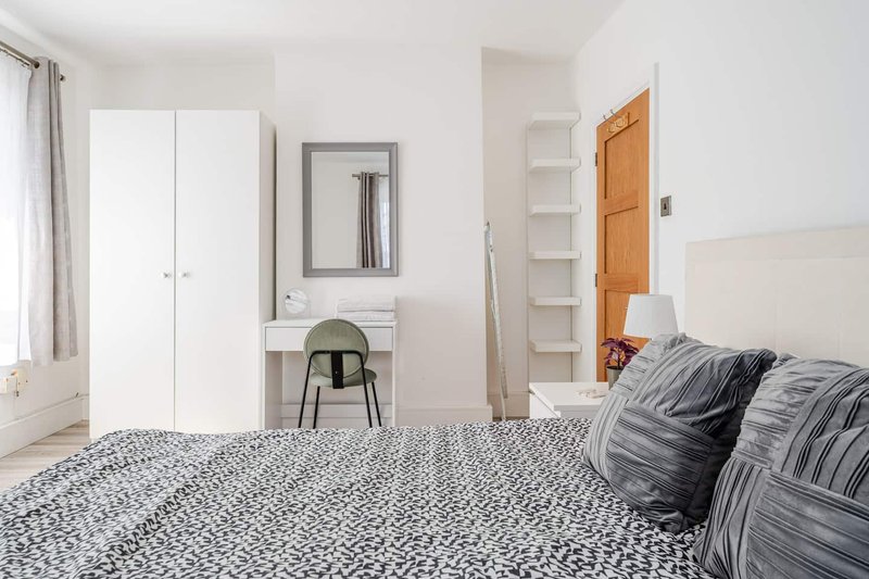 Bright bedroom with double bed, white wardrobe, desk, mirror and wooden door