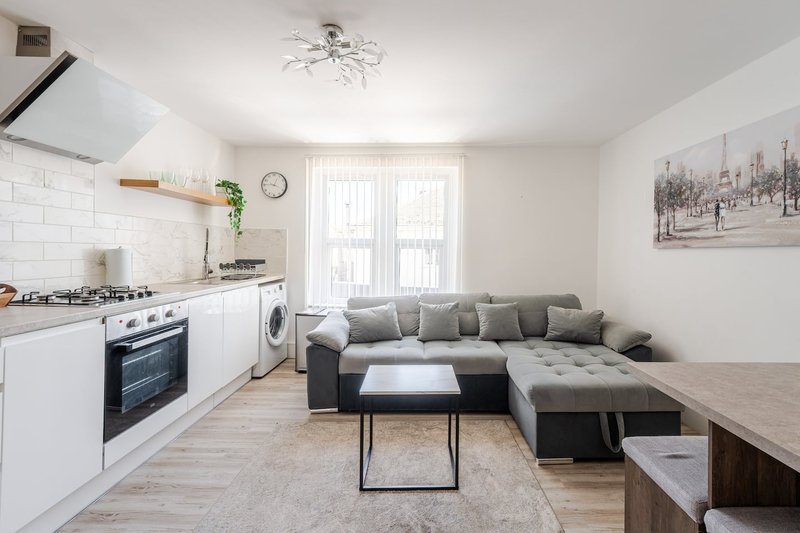 Open-plan kitchen and living room with white cabinetry, grey sofa, and large windows