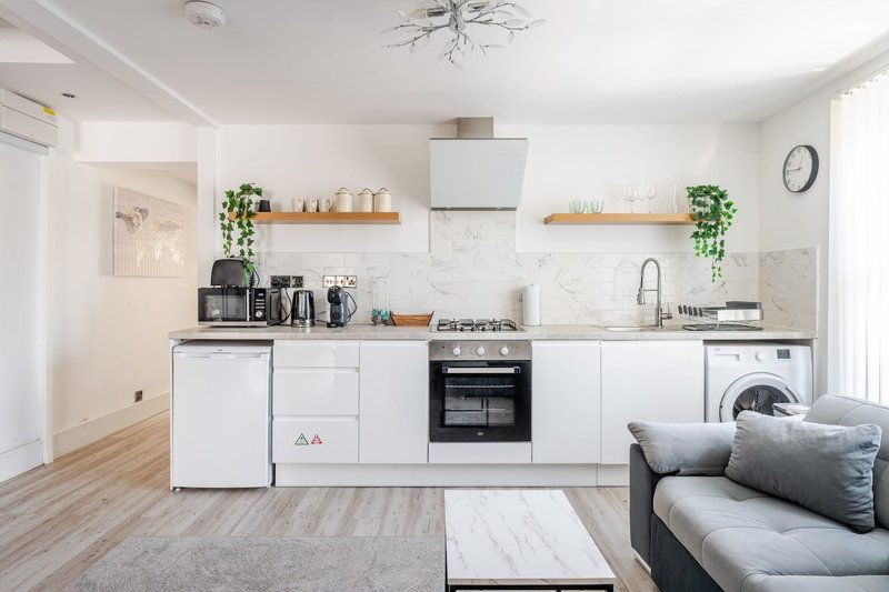 Modern open-plan kitchen with white cabinetry, marble backsplash, wooden shelves, and integrated appliances