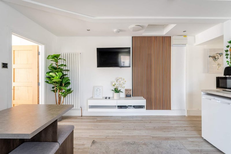 Modern open-plan living room with wooden flooring, wall-mounted TV, and contemporary furnishings