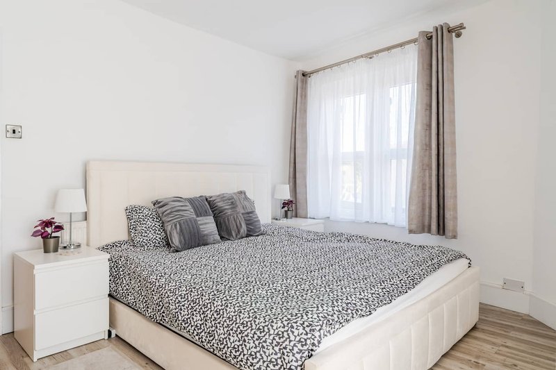 Bright bedroom with double bed, patterned bedding, white nightstand, and sheer curtains