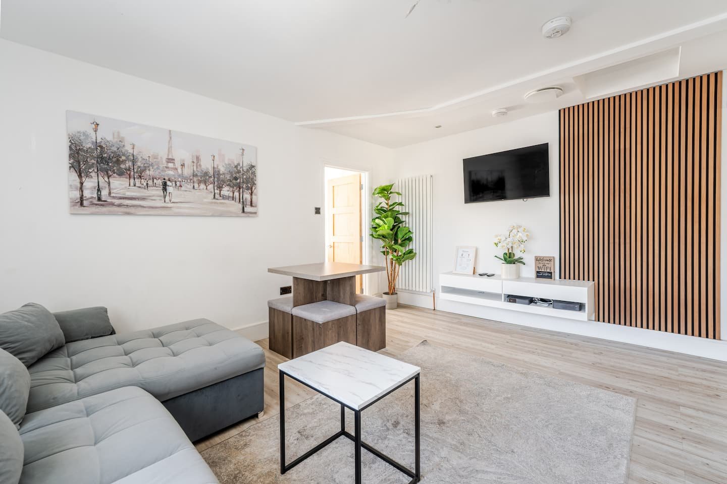 Modern living room with grey sofa, wooden shelving, wall-mounted TV, and decorative artwork