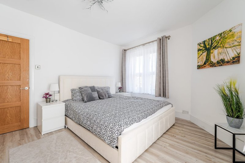 Bright bedroom with double bed, white headboard, wooden door, and patio doors with curtains
