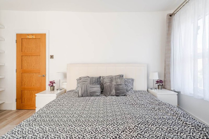 Bright bedroom with white bed frame, patterned bedding, wooden door and large window