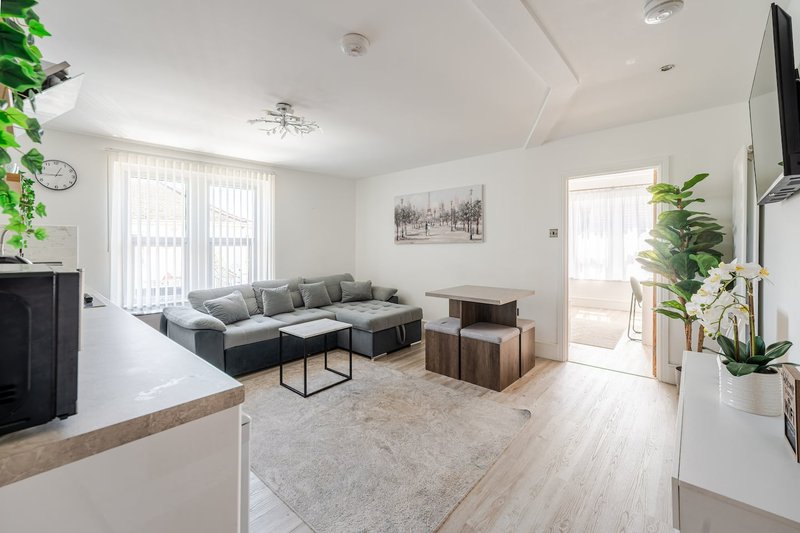 Bright open-plan living room with grey corner sofa, wooden floor, and large windows