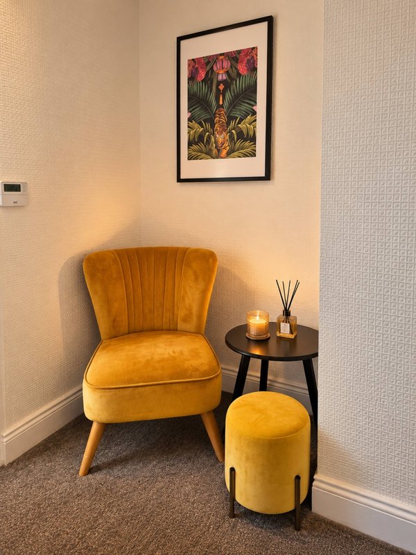 Cozy corner with golden velvet chair, side table, candle, and framed wall art