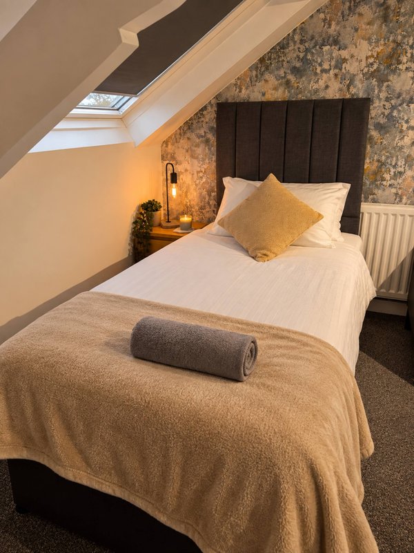 Attic bedroom with single bed, black headboard, skylight window and bedside lamp
