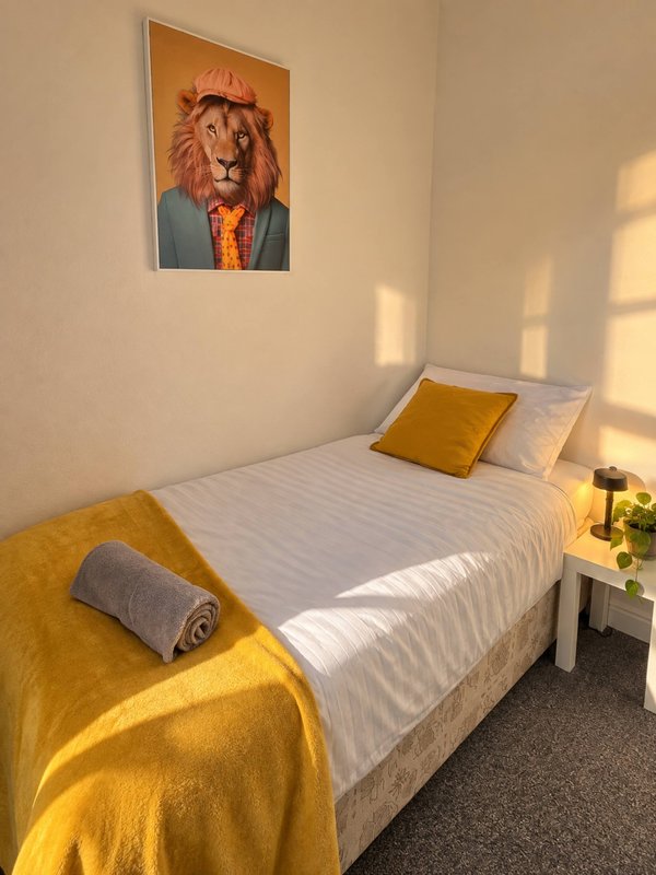 Bedroom with single bed, yellow bedding, framed lion artwork on wall
