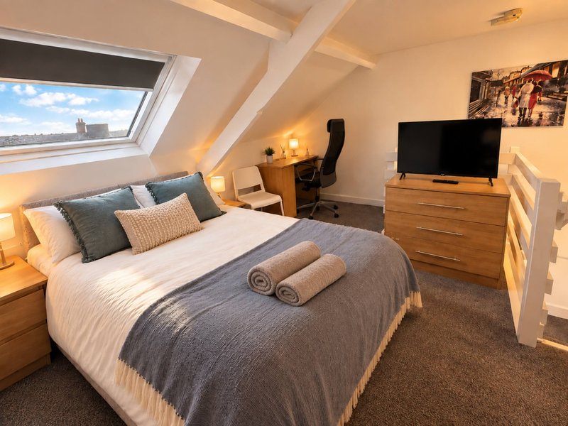 Modern attic bedroom with double bed, skylight window, TV on dresser, and warm lighting