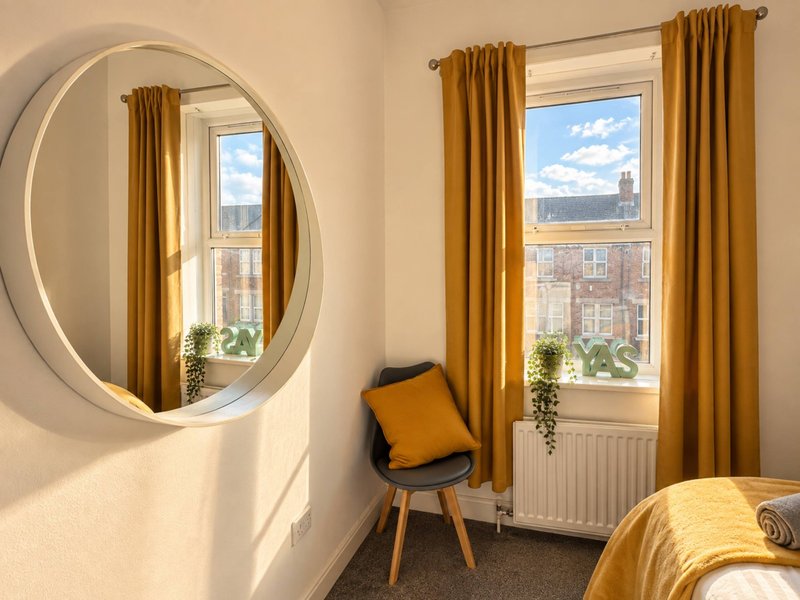 Bright bedroom with round mirror, gold curtains, chair, radiator and city views