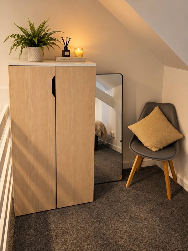 Attic bedroom corner with wooden wardrobe, mirror, chair, potted plant and warm lighting