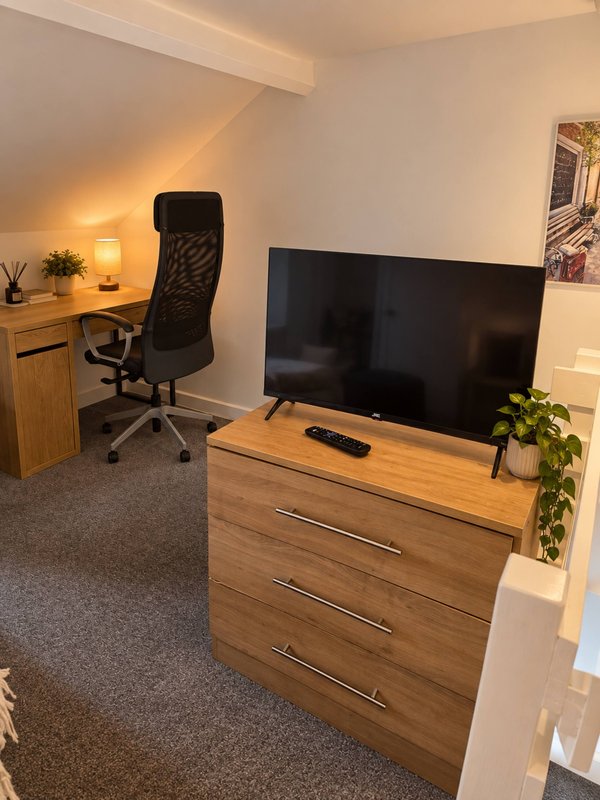 Studio workspace with wooden desk, office chair, TV on dresser, and work area with lamp