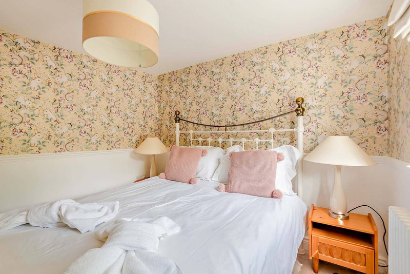 Bedroom with floral wallpaper, metal bed frame, white bedding, pink cushions and bedside lamps