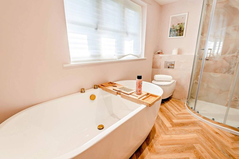 Spacious bathroom with white bathtub, wooden bath tray, shower enclosure and window