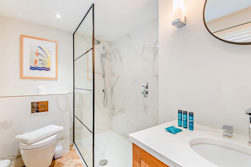 Modern bathroom with marble shower, white vanity, wooden cabinet and framed nautical artwork