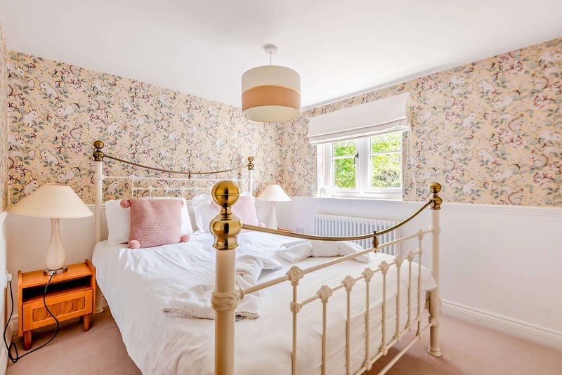 Bedroom with brass bed frame, floral wallpaper, pink bedding, and window with garden view